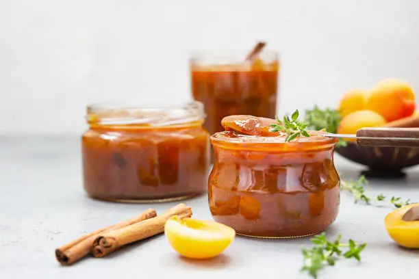 Homemade organic apricot jam in glass jars, ripe apricots, cinnamon and thyme on grey concrete background.