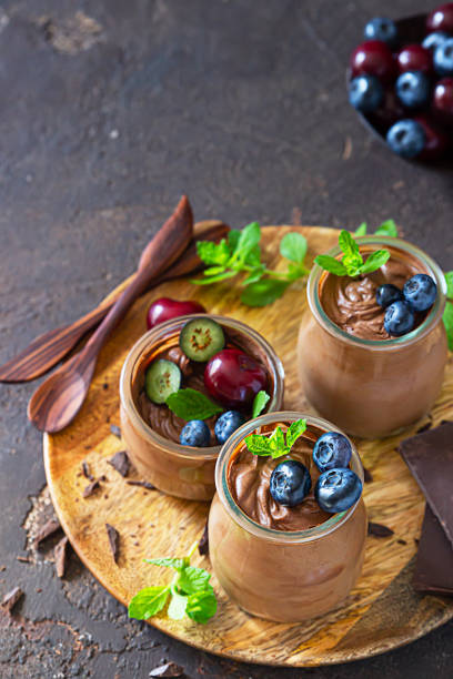 istock Portion jars with chocolate mousse or pudding decorated with sweet cherry, blueberry and mint and pieces of dark chocolate. Selective focus. Dark background. 1266429202
