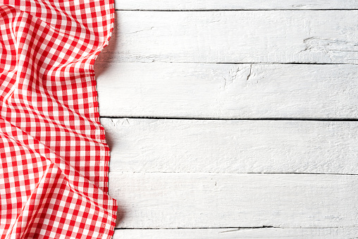 Red checkered tablecloth on white wooden table. Top view