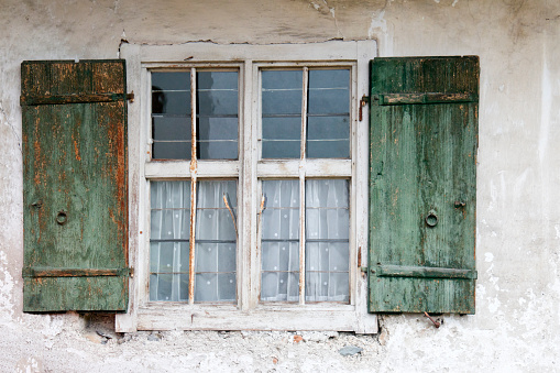 old wooden window with open shutter and roll up jalousie, bright cement wall with rough surface, no people