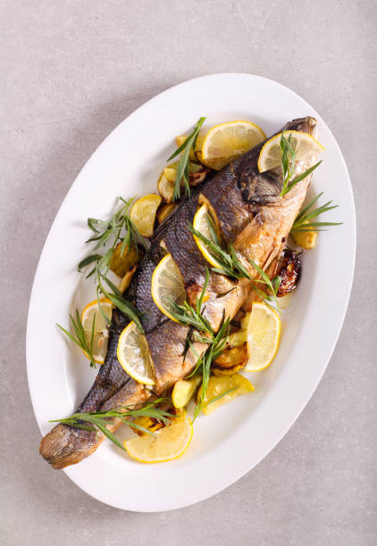 Baked sea bass fish with tarragon and lemon Baked sea bass fish with tarragon and lemon on plate sea bass stock pictures, royalty-free photos & images