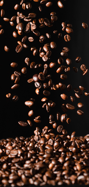 Falling coffee beans isolated on black background. Vertical photo
