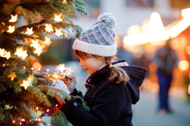 little cute kid girl having fun on traditional christmas market during strong snowfall. happy child enjoying traditional family market in germany. schoolgirl standing by illuminated xmas tree. - hot chocolate hot drink heat drinking imagens e fotografias de stock