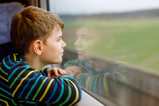 Adorable kid boy traveling by train. Happy smiling child looking out of the window during train moving. Kid dreaming and wondering. Family vacations and journey trip