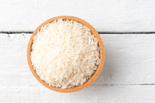 istock Uncooked white rice in bowl on rustic wooden table. Top view 1266447472