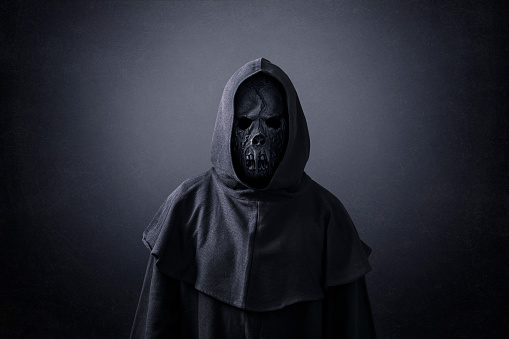 Scary figure in hooded cloak in the dark