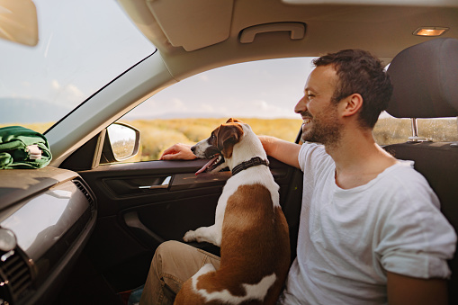 Photo of a smiling young man and his dog riding in a car on a bright summer day.
