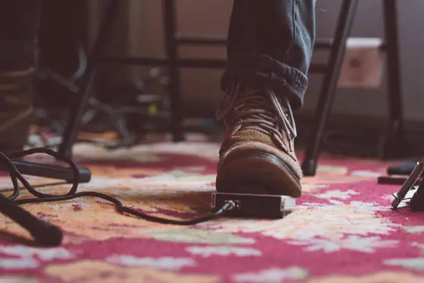 Musician's foot on equipment pedal. Moody atmosphere on a textured red carpet.