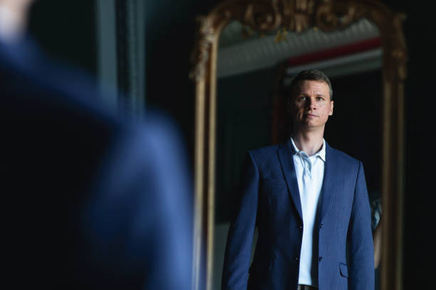 istock Handsome stylish man in blue jacket at home looking at mirror. 1266455398