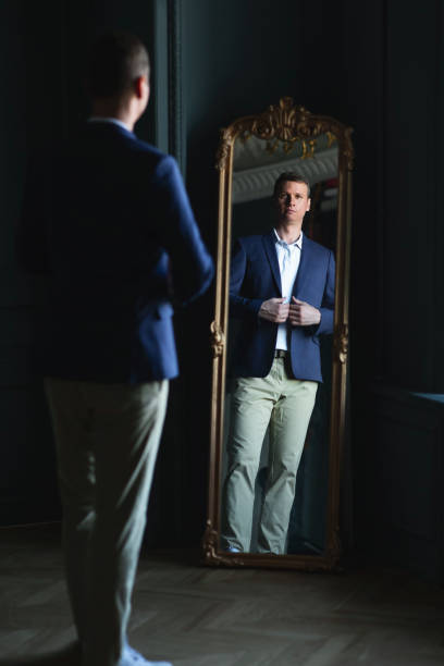 istock Handsome stylish man in blue jacket at home looking at mirror. 1266455399