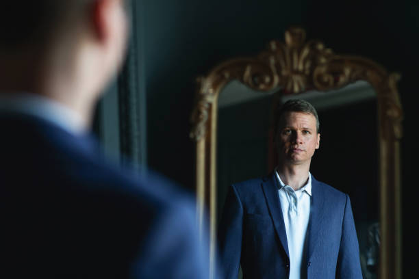 istock Handsome stylish man in blue jacket at home looking at mirror. 1266455400