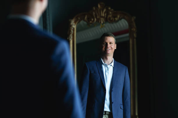 istock Handsome stylish man in blue jacket at home looking at mirror. 1266455407