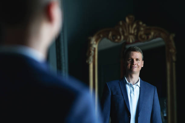 istock Handsome stylish man in blue jacket at home looking at mirror. 1266455412