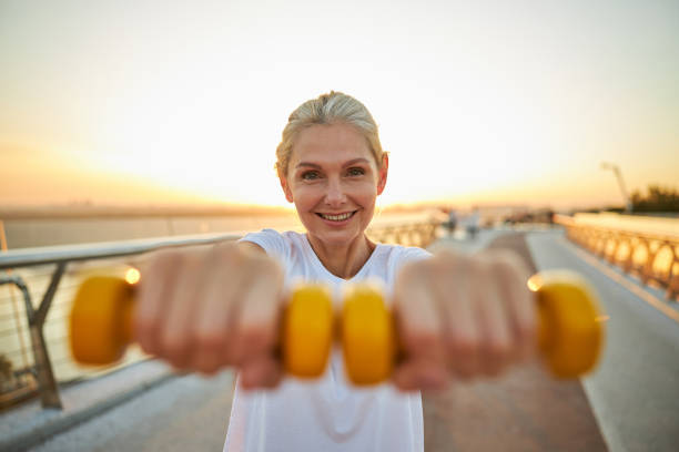 istock Cheerful woman doing exercise with dumbbells outdoors 1266458819