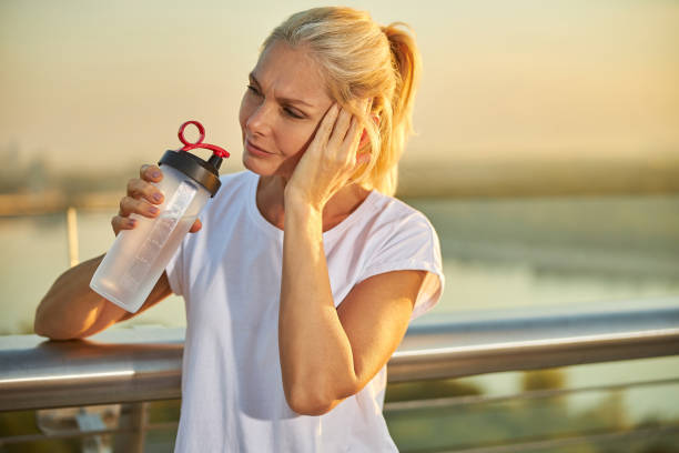 istock Unhappy woman drinking water while having headache 1266458848