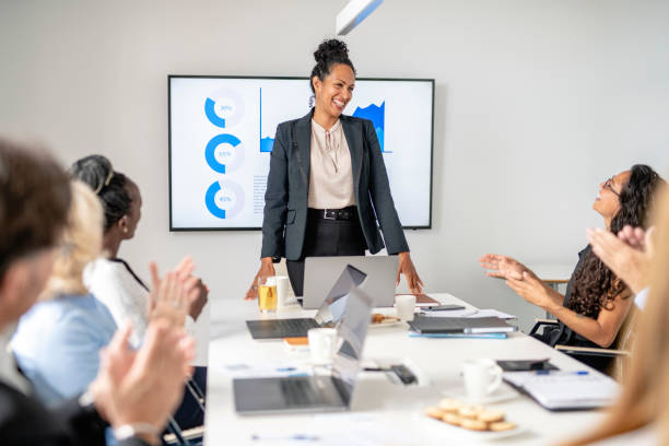 Multi-Ethnic Executive Team Applauding Female CEO in Meeting Personal perspective of Hispanic business professional in early 40s smiling as colleagues applaud successful presentation in office board room. local office manager stock pictures, royalty-free photos & images