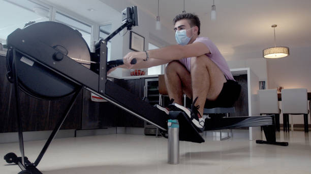 istock Young cuban guy using a mask rowing machine in the house 1266463945