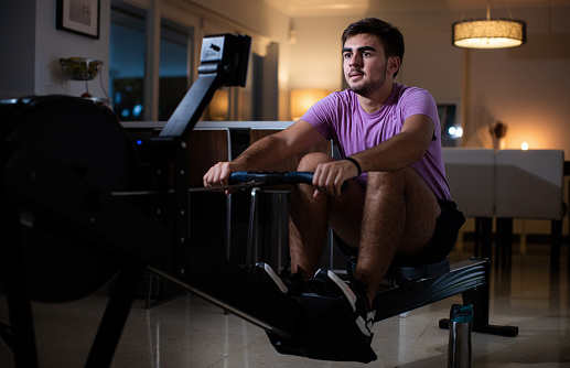 Young cuban man rowing machine exercises sets in the kitchen