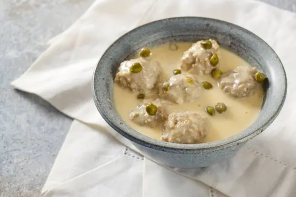 Koenigsberger Klopse or boiled meatballs in a white bechamel sauce with capers, traditional Polish and German dish in a gray bowl on a white napkin, selected focus, narrow depth of field