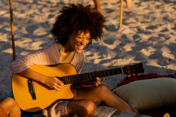 istock Young mixed race woman playing guitar and laughing on beach 1266465668