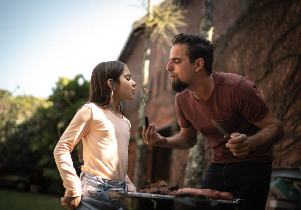 Father and daughter blowing a slice of hot meat in a barbecue Father and daughter blowing a slice of hot meat in a barbecue barbecue grill photos stock pictures, royalty-free photos & images
