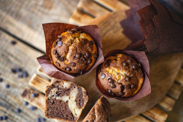 istock Soft and moist chocolate muffins with dark chocolate chips in wooden box, rustic table. Homemade baked twisted cupcakes. 1266476445