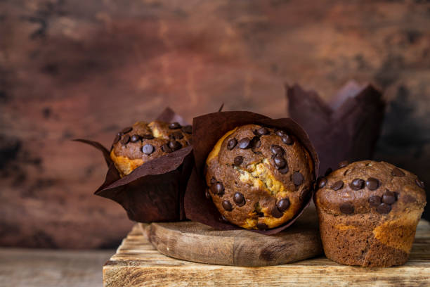 istock Soft and moist chocolate muffins with dark chocolate chips in wooden box, rustic table. Homemade baked twisted cupcakes. 1266476483