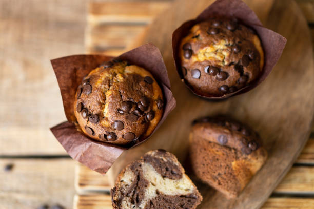 istock Soft and moist chocolate muffins with dark chocolate chips in wooden box, rustic table. Homemade baked twisted cupcakes. 1266476491