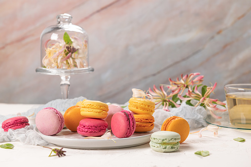 Colorful french macaroon cakes. Macaroons with honeysuckle flowers and tea on white table background. Selective focus