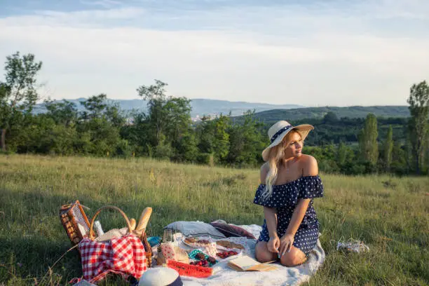 Photo of A girl with a straw hat and a polka dot dress is sitting on a picnic blanket