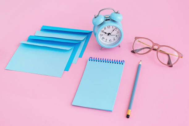 istock Blue correspondence envelopes, clock and notebook on pink background with copy space. Back to school or work concept. 1266481299