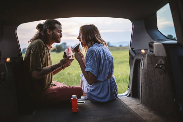 Couple eating watermelon in the car trunk Happy young couple sitting in car trunk and eating watermelon hipster car stock pictures, royalty-free photos & images