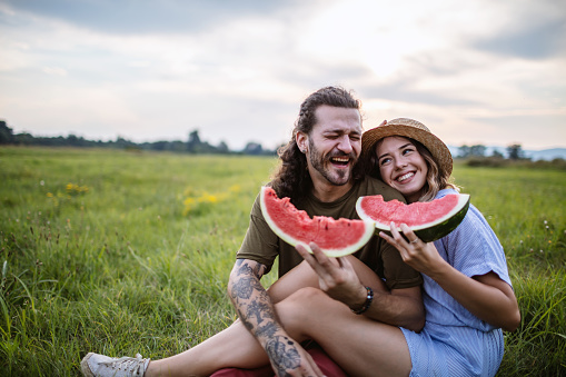 Cheerful young couple having fun while eating watermelon during picnic day in nature