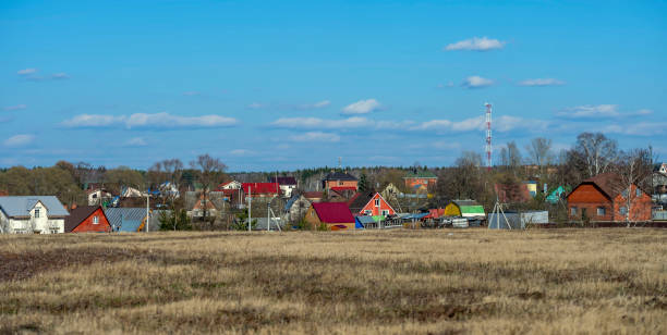 Typical Russian village in the Moscow region, Russia. Spring field and cumulus clouds, multi-colored facades of country houses.