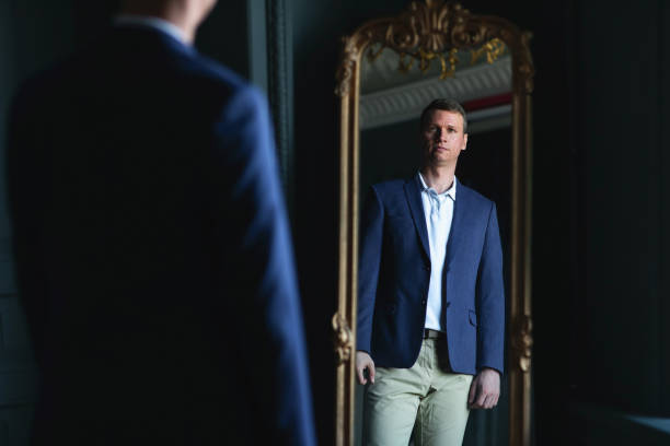 istock Handsome stylish man in blue jacket at home looking at mirror. 1266492707