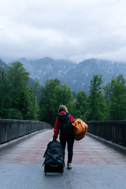 istock Young woman backpacker pulls luggage across bridge over a mountain river in the forest 1266493592