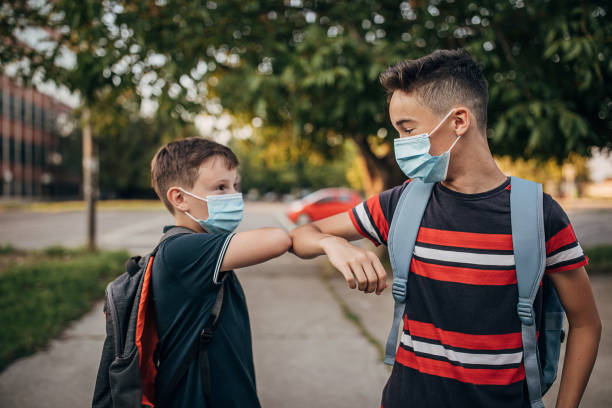 istock Two schoolboys with surgical masks greeting with elbow bump outside their elementary school building 1266506580