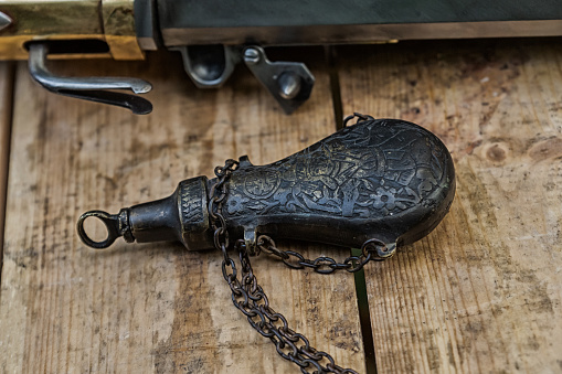 old vintage iron powder flask for charging musket closeup on wooden background