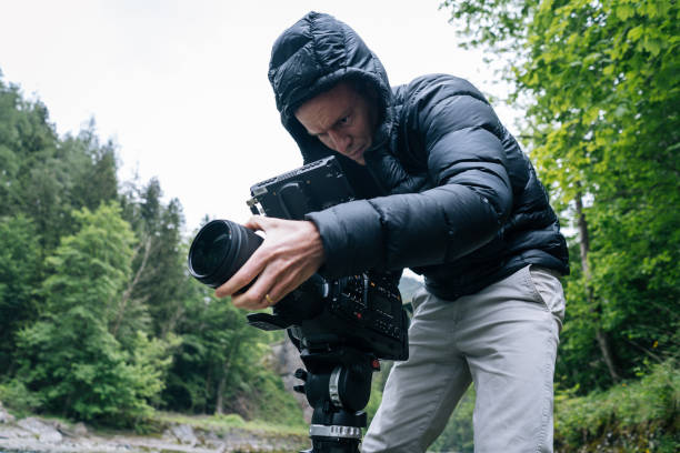 istock Man with film camera mounted on a tripod shoots a moving river 1266513966