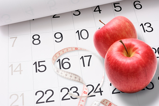 High angle view of two red apples with a measuring tape on a calendar.\nDiet concepts.