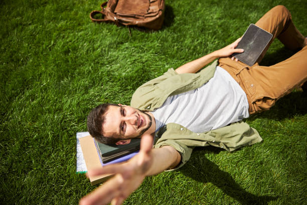 istock Man lying on the grass with his head on textbooks 1266545803