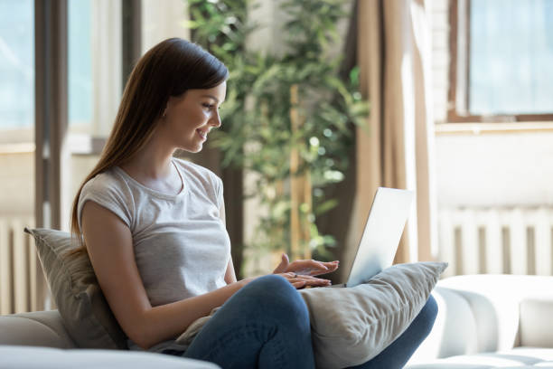 istock Happy smiling young female sitting on couch with laptop 1266551900