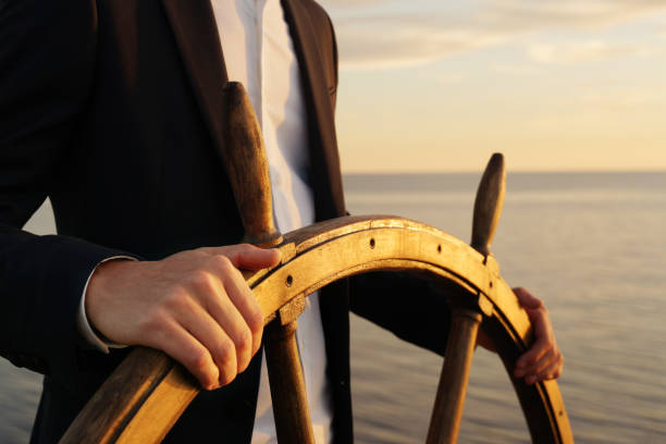 Businessman holding ship rudder and navigates in sunset light.