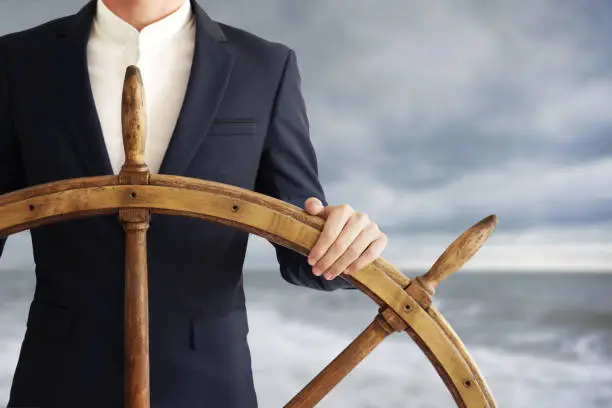 Businessman holding ship wheel and navigates in storm.