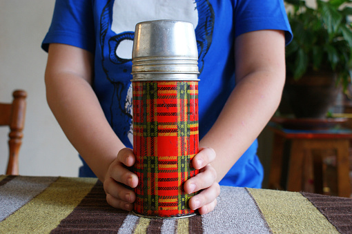 Vintage thermos. An old retro plaid thermos in the hands of a child