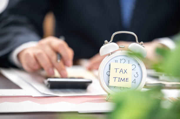 Alarm clock with tax time note and Businessmen using calculators. Alarm clock with tax time note and Businessmen using calculators. tax season photos stock pictures, royalty-free photos & images