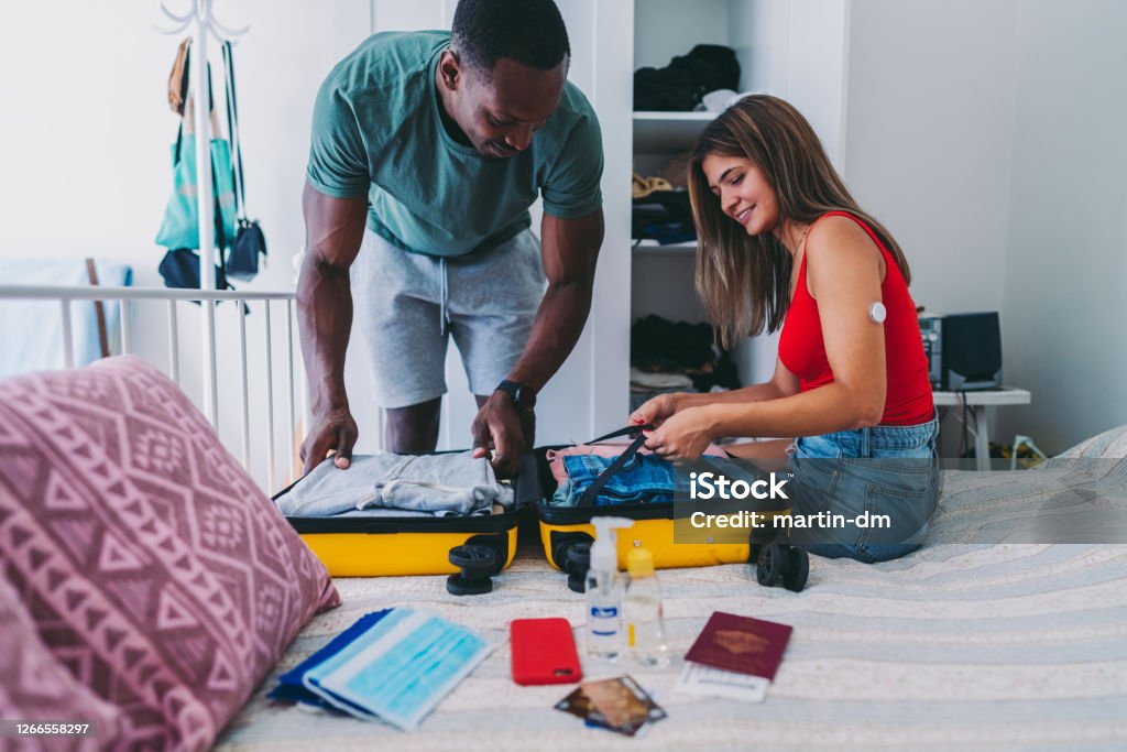 Couple packing suitcase for travel, COVID-19 summer Couple packing suitcase for summer trip, including face masks and travel-sized antibacterial hand gels due to COVID-19 Packing Stock Photo