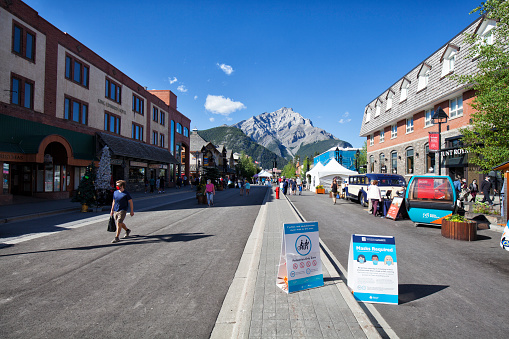 Banff, Alberta, Canada - August 9, 2020: Street view of famous Banff Avenue on a sunny afternoon during Covid-19 Pandemic. Warning signs in the middle of the street.