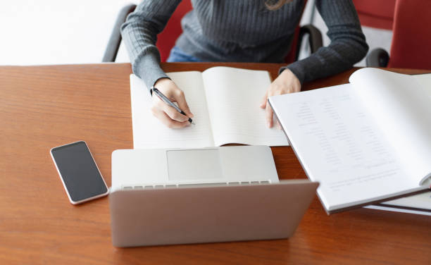 istock Young business woman sitting at table and taking notes in notebook, On table is laptop, Smartphone and cup of coffee, Student learning online, Back to school education knowledge college university 1266563076