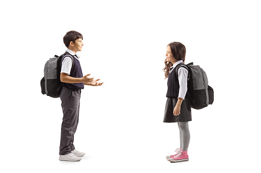 Full length profile shot of a schoolboy gesturing with hands and talking to a schoolgirl isolated on white background